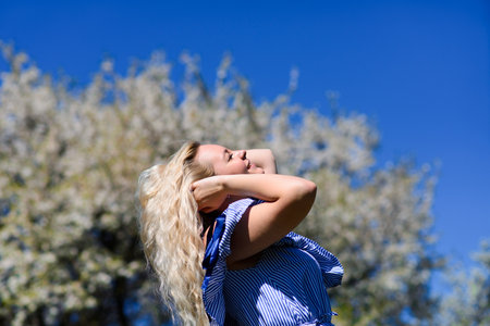 A young blonde girl is looking at the beautiful blue sky and reaches for the sky with her hands. Beautiful female admires nature.の写真素材