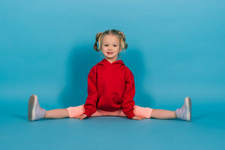 Beautiful girl sits on a splits isolated on blue backgroundの写真素材