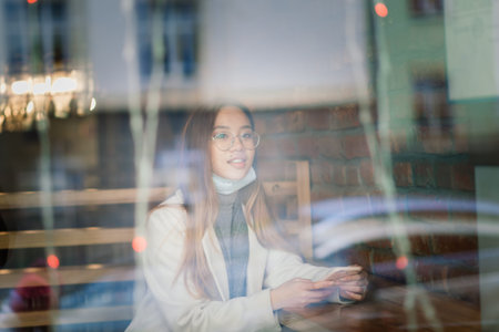 Young Asian businesswoman with mask using phone and sitting with distance outside coffee shop