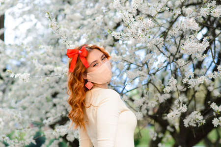 Girl, young woman in a protective sterile medical mask on her face in the spring garden.の写真素材