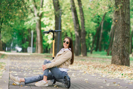 Young woman riding an electric scooter in autumn park. Green transport, traffic jam problems.の写真素材