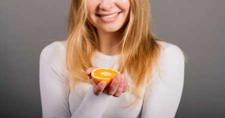 Smiling woman eating orange in studio, half fruit, blonde long hair.の写真素材