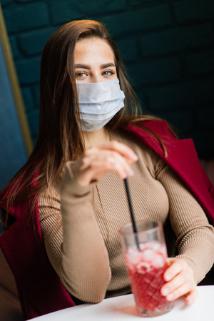 Close up portrait of a caucasian female wearing a medical mask and standing in the street against background of a cafeの写真素材