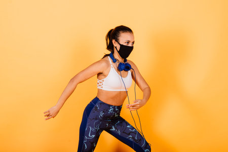 Portrait of fit african woman wearing face mask. Sporty woman in fitness wear standing on a yellow...