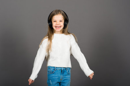 Cute child girl in headphones enjoying happy dance music, smile, posing on grey studio background...