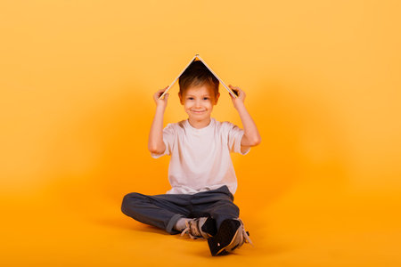 Portrait of little schoolboy with book on yellow background, studio