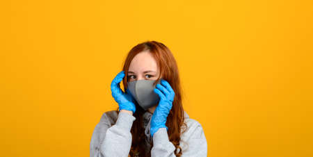 Portrait of a girl in a mask, which puts on rubber gloves. Yellow background.の写真素材