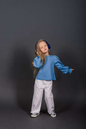 Smiling little girl in headphones on a grey background. The child listens to music, plays and learns online. Electronic digital training.の写真素材