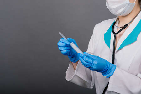 Serious female doctor in a medical mask holding syringe and vaccine isolated on greyの写真素材