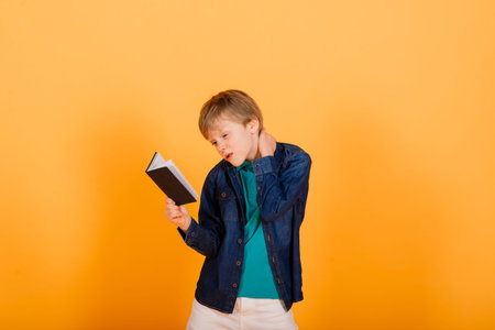 Smart ginger-haired young schoolboy with notebook isolated over yellow background, studio