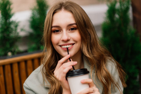 Very beautiful young woman, sit in Cafe and drink coffee or tea with croissant, street front viewの写真素材
