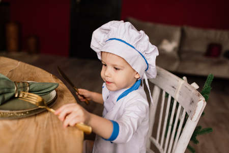 Healthy eating concept. Happy little boy is cooking in kitchen on a sunny summer day. Toddler baker on a picnic eats bread and bagels in a white apron and hatの写真素材