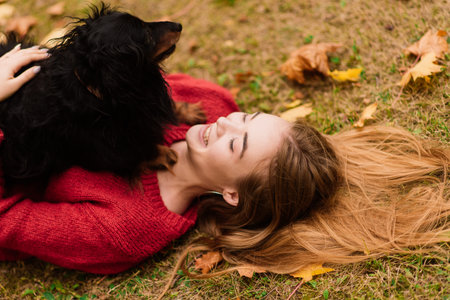 Woman hugging dog in the summer park. Cheerful lady with long dark hair hugs and strokes friendly...