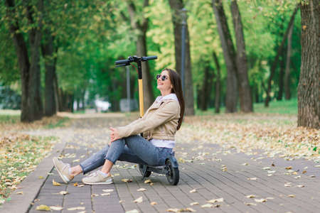 Young beautiful stylish woman riding electric scooter in autumn park, ecological transportの写真素材