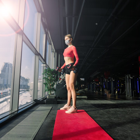 Coronavirus covid-19 prevention, fitness girl with a medical mask holding dumbbell . Fighting viruses.の写真素材