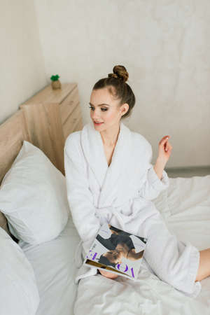 Minsk, Belarus - 01.18.2021. Young adult brunette woman reading a brochure on hotel room bed.のeditorial素材