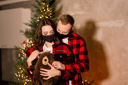 Attractive man and young woman wearing face masks celebrating new year 2021 at home quarantine,...