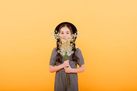 Portrait of cute little girl with flower bouquet in the studio on yellow background. Congratulation, spring or happy holiday concept. Copy space for textの写真素材