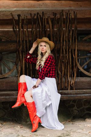 Minsk, Belarus - 09.12.2020. Beautiful blonde young female in elegant hat near the old wooden fence and on field with ponies, country brideのeditorial素材