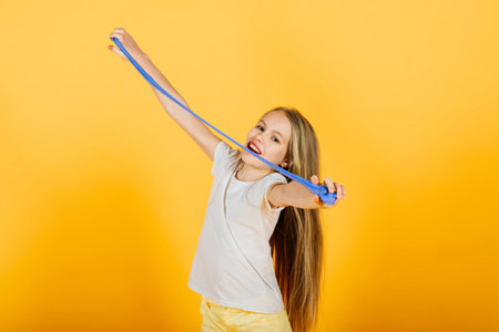 Young girl playing with blue slime on yellow background, studio shot