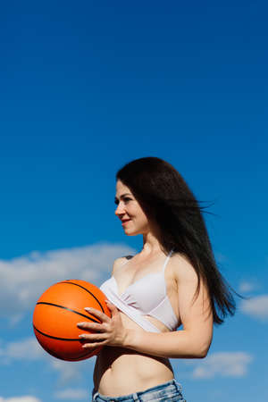 Young athletic female, in a top and sweatpants, playing with ball on basketball court outdoors.の写真素材