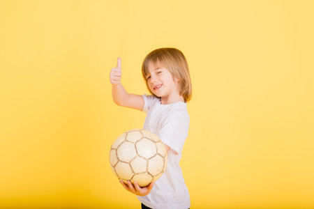 Cute boy is holding a football ball made of genuine leather isolated on yellow background. Soccerの写真素材