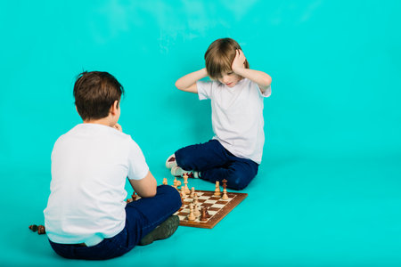 Two serious boy playing chess in studio, blue backgroundの写真素材