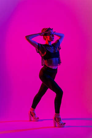 Beautiful female dancer wearing black and high heels while performing pole dance tricks, neonの写真素材