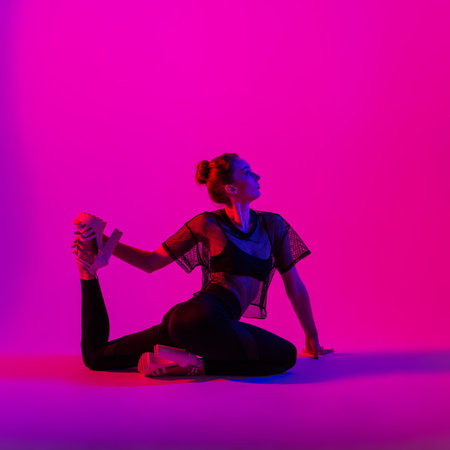 Beautiful female dancer wearing black and high heels while performing pole dance tricks, neon