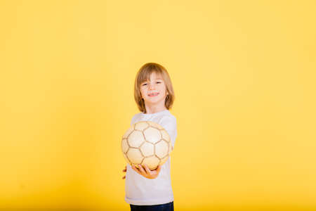 Portrait of a boy holding soccer ball, studio yellow backgroundの写真素材