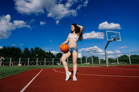 Young athletic female, in a top and sweatpants, playing with ball on basketball court outdoors.の写真素材