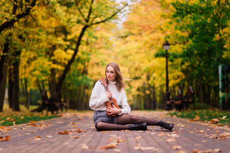 Beautiful woman playing ukulele guitar at outdoor in an autumn forestの写真素材