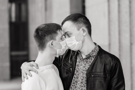 Young gay couple wearing medical mask, hugging and kissing at city.