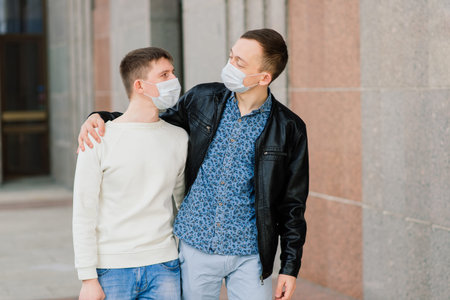 Young gay couple wearing medical mask hugging at the city.