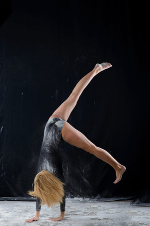 Beautiful blonde girl wearing black gymnastic bodysuit covered with clouds of the flying powder