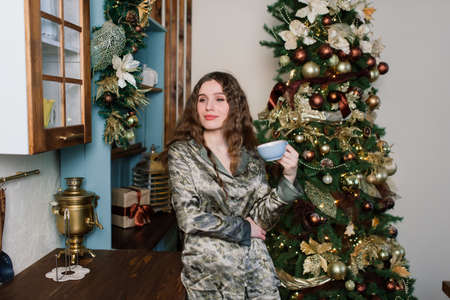 Happy emotional surprised young woman by a Christmas tree in cozy living room, concept of happinessの写真素材