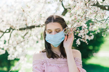 A young female in a medical face mask to avoid the spread virus between flowering trees.の写真素材