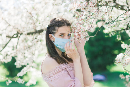 A young female in a medical face mask to avoid the spread coronavirus between flowering trees.の写真素材
