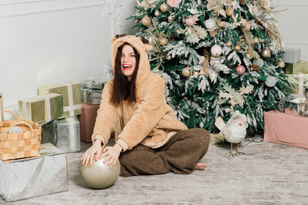 Woman dressing Christmas tree, smiling, sitting in a new year interiorの写真素材