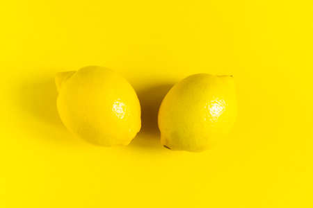 Juicy lemons on a bright yellow background, citrus minimal concept. Flat lay, top view, copy space.の写真素材
