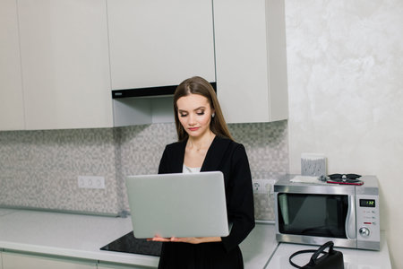 Woman in black suit smiling at a laptop in kitchen