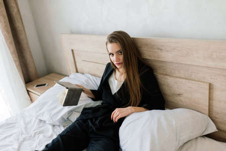 View of woman lying on a sofa and reading book at homeの写真素材