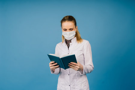 Photo of beautiful doc lady wear a protective mask white lab coat isolated blue color backgroundの写真素材