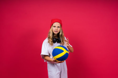 Portrait of a cute eight year old girl in volleyball outfit isolated on a red backgroundの写真素材