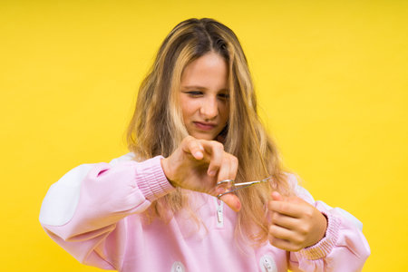 Child adorable girl hairdresser cutting long blonde hair with metallic scissors on yellowの写真素材