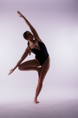 Young slim female in black bodysuit makes yoga stretching exercise on white studio wall background.の写真素材
