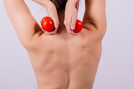 Healthy young woman holding tomatos over her eyes, laughing, bare shoulders, topless.の写真素材