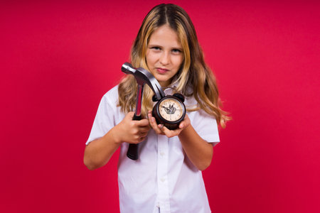 Young blonde girl holding alarm clock and hammer smiling and laughing hard out loud.の写真素材