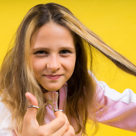 Child adorable girl hairdresser cutting long blonde hair with metallic scissors on yellowの写真素材