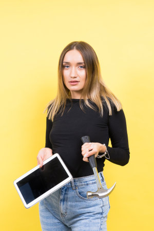 Woman with tablet and hammer, Studio lighting yellow background isolated, copy spaceの写真素材